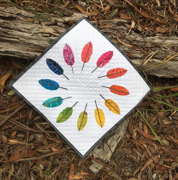 a wreath style foundation pieced pattern featuring feathres in rainbow colours sewn in fabrics to create a mini quilt
